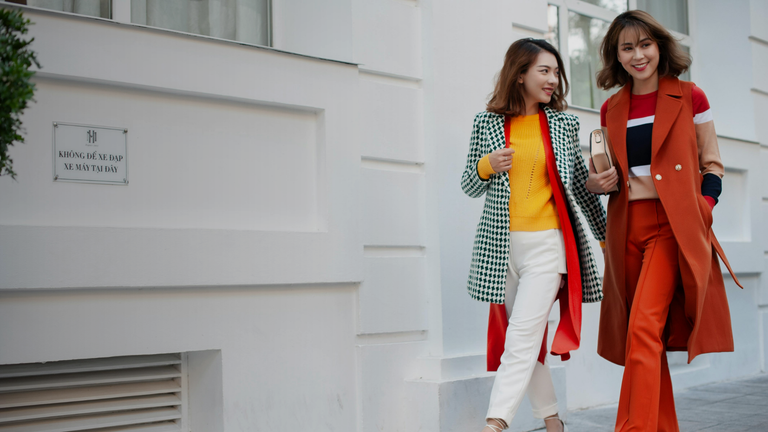 Stylish women in colorful coats walking city street natural light